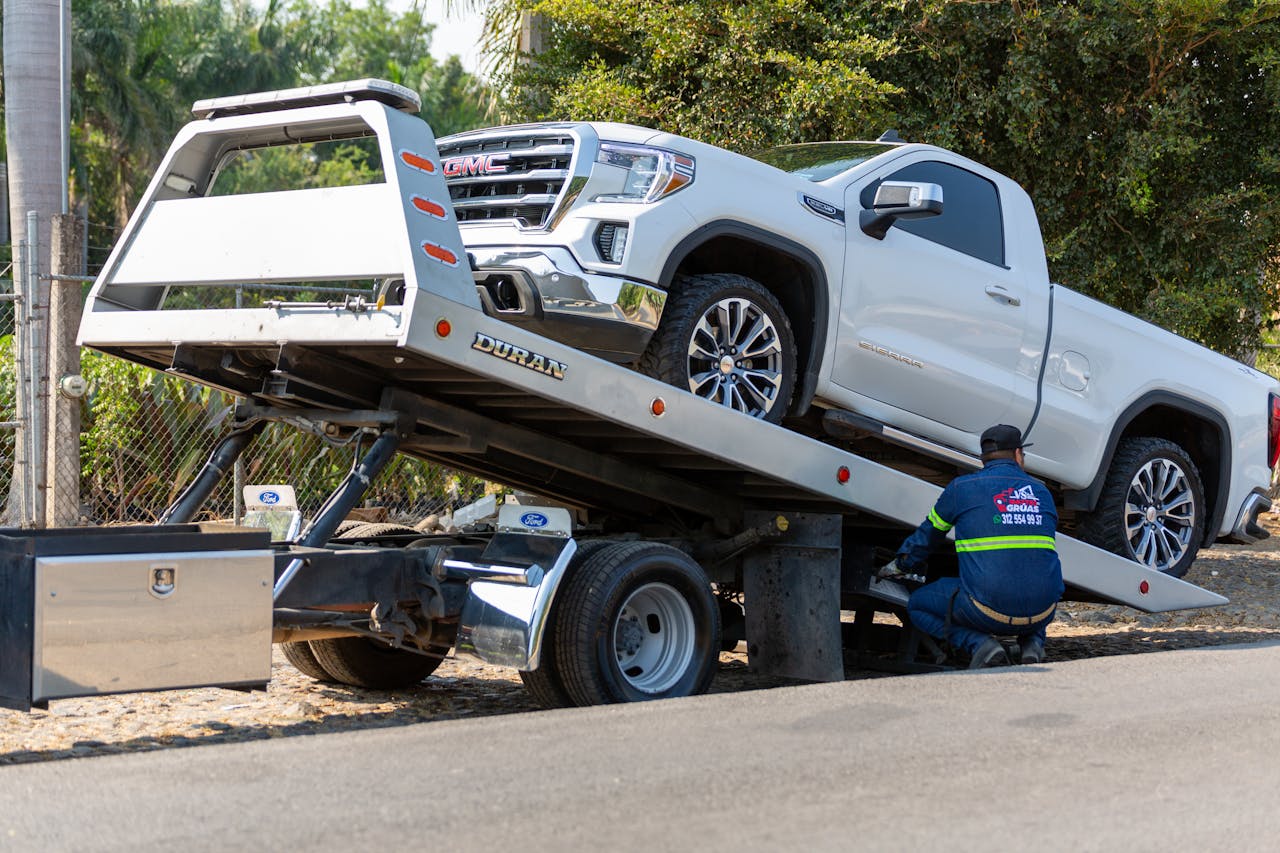 pexels photo 17429097 Tow truck operator loading white GMC pickup truck on street in daytime.